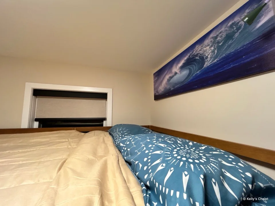 Blue patterned pillows and pale bedding beneath ocean wave artwork in Bedroom II at Kelly’s Chalet