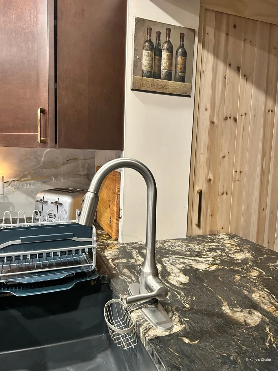Kitchen sink and curved tap beside a stone patterned counter and timber door
