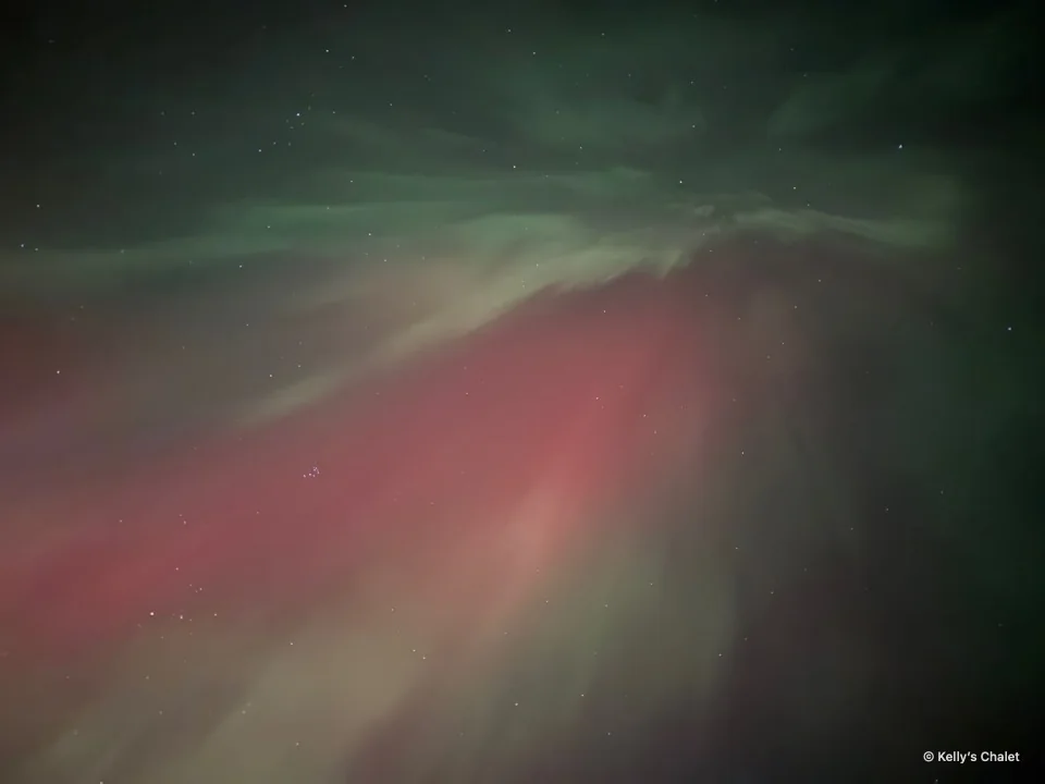 Red and green aurora spreading across the Grand Beach area night sky, photographed away from Kelly’s Chalet