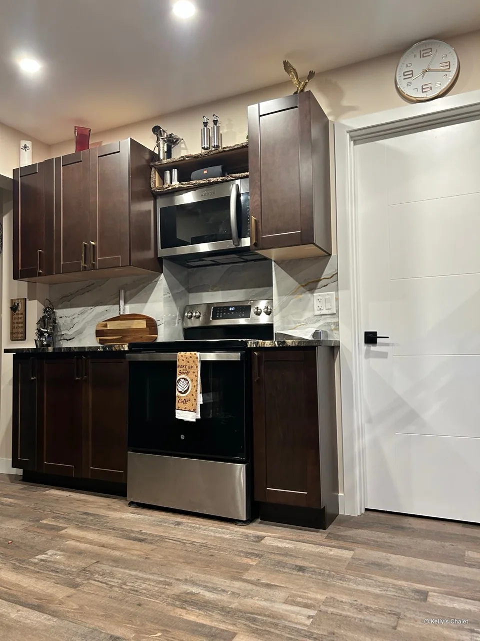 Stove and microwave between dark kitchen cabinets with a pale veined backsplash